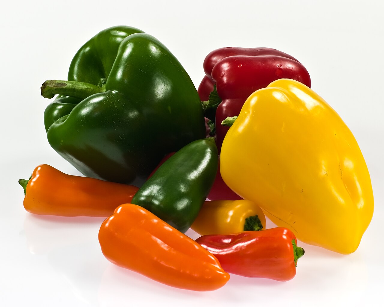 Сладкие перцы Capsicum annuum разной формы и окраски: зелёные, красные, жёлтые и оранжевые плоды на светлом фоне
